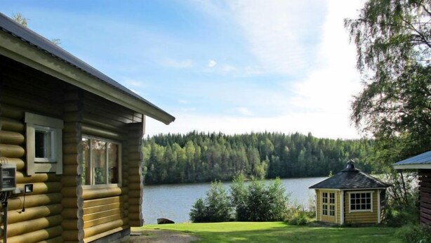 A log cabin with a view of a lake and forest.
