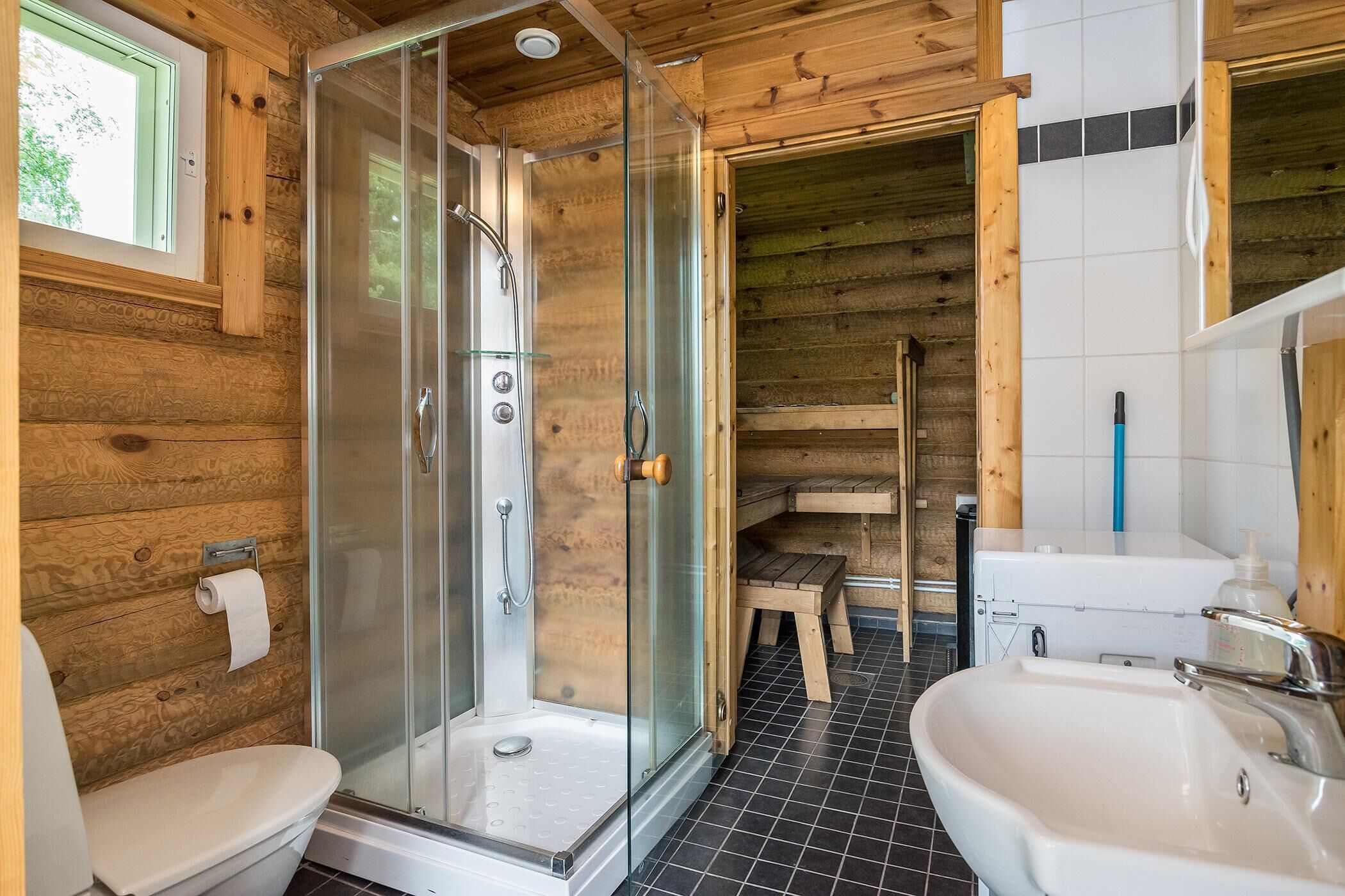 A wooden cabin bathroom with a glass shower, two sinks, and a toilet.