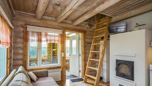 A cozy log cabin interior with a sofa, fireplace, and a ladder to the upper floor.