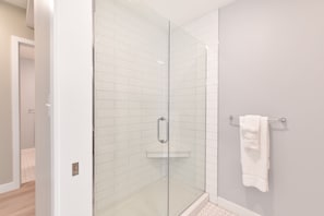 A modern bathroom with a glass shower enclosure, white tiled walls, and a visible towel rack. - Harmony Medical Suites Longwood (Boston)