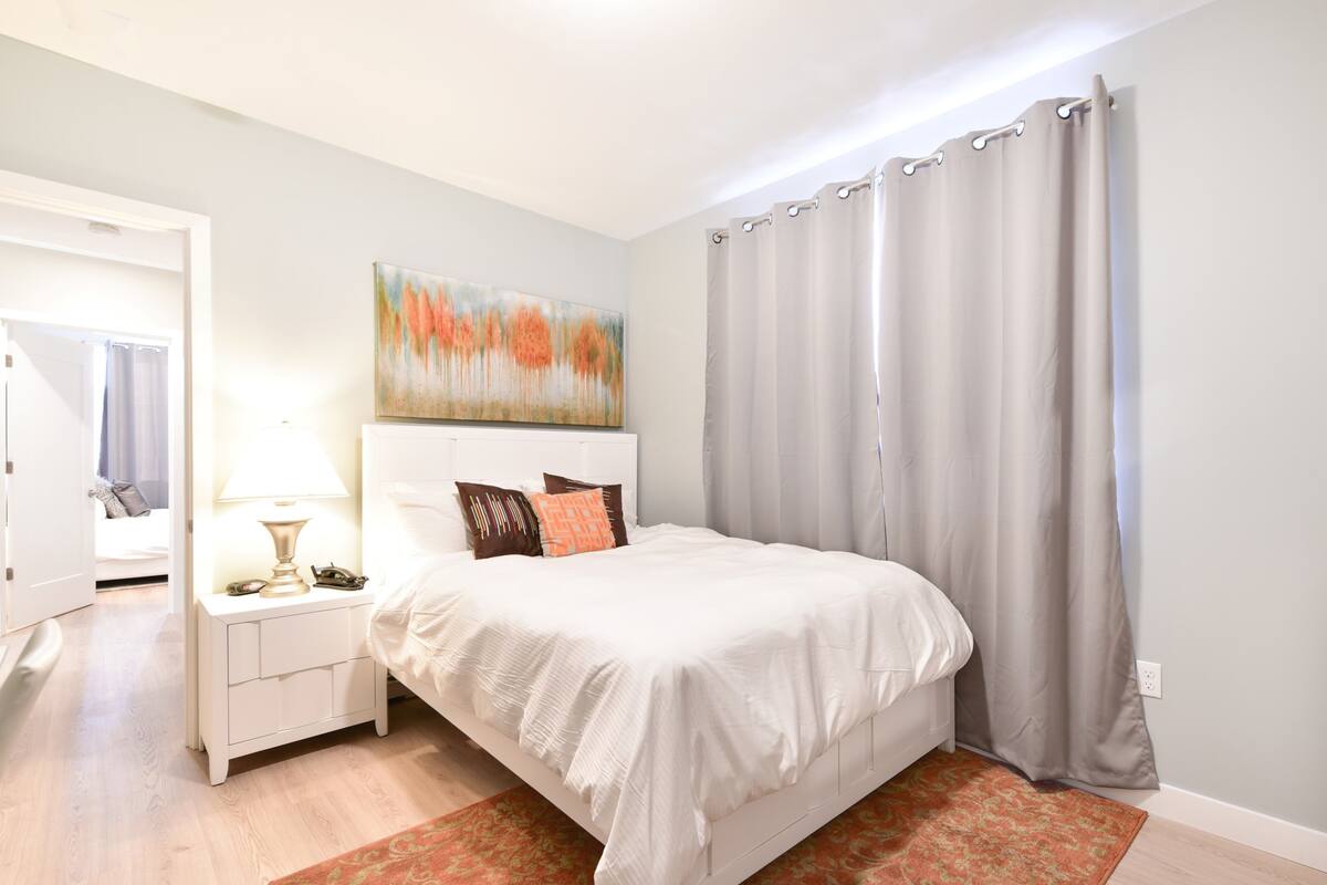 A bedroom with a bed, nightstand, lamp, and a painting on the wall.