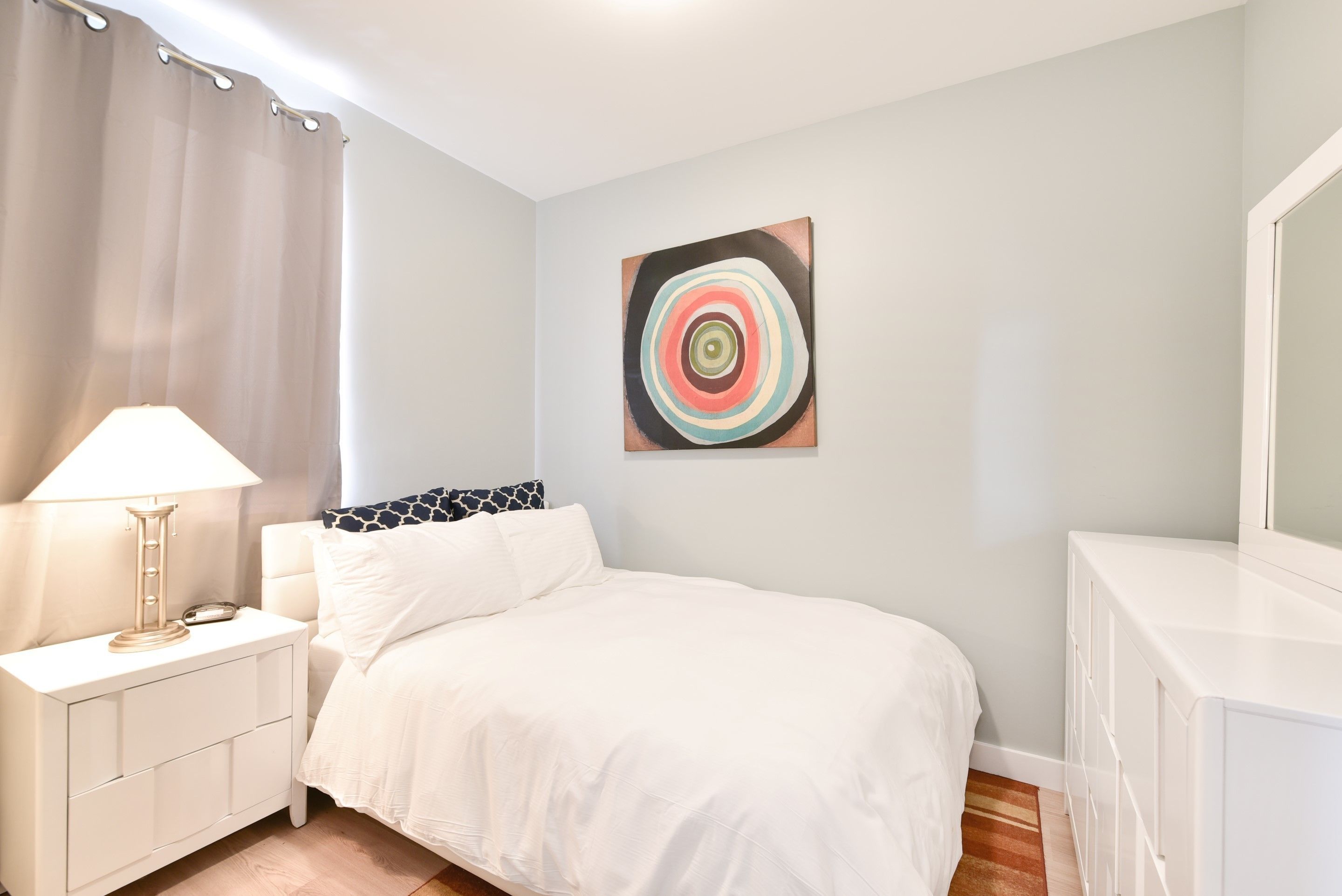 A bedroom with a bed, bedside table, lamp, and a wall art piece.