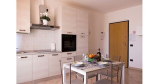 A modern kitchen with white cabinets, a black oven, and a dining table set for two. - Residence Le Groane (Garbagnate Milanese)