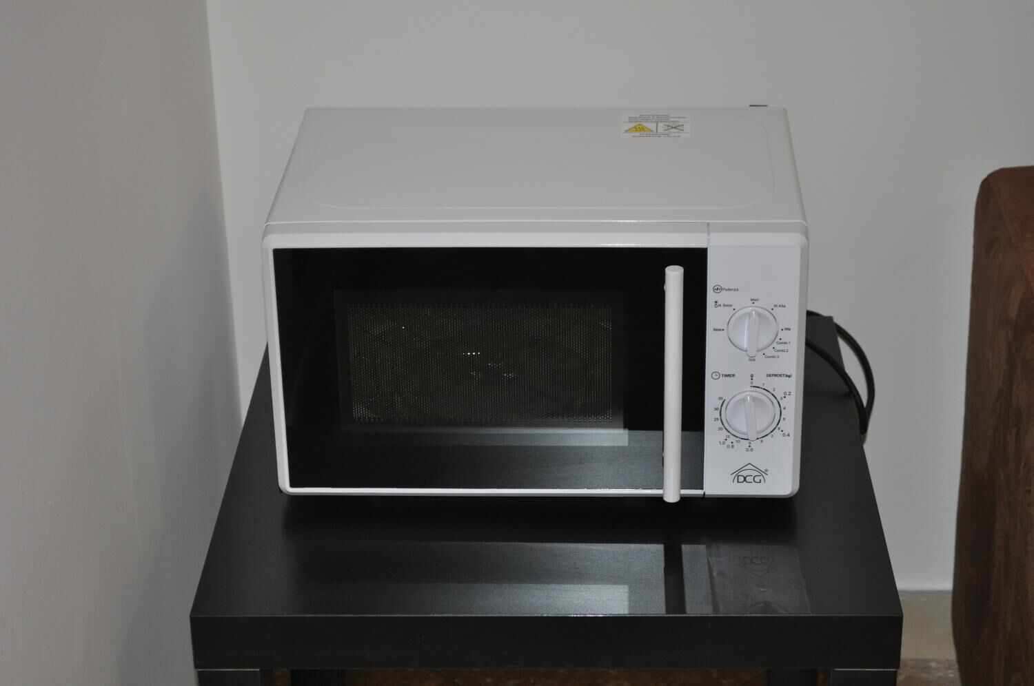 A white microwave on a black table against a white wall.