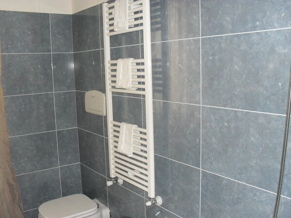 Un baño con paredes de baldosas oscuras, un inodoro blanco y un toallero blanco con toallas.