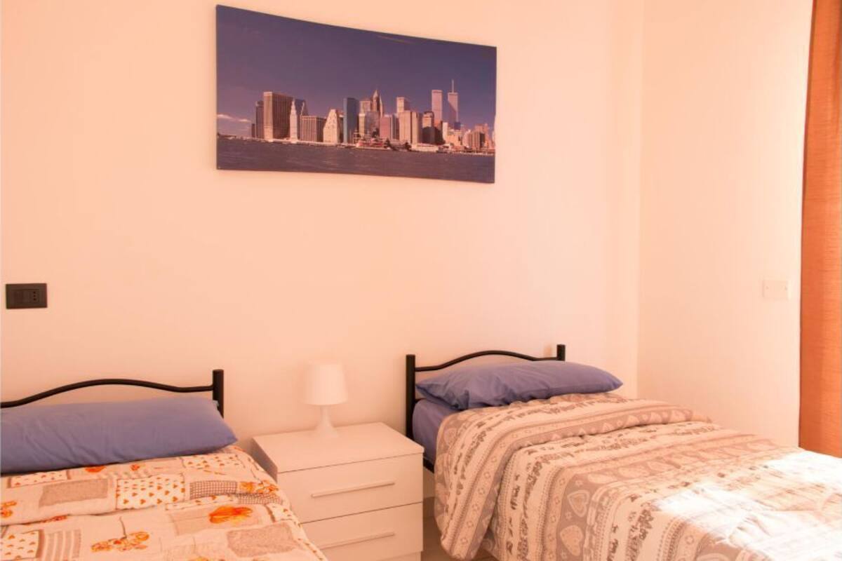 Une chambre avec deux lits, un tableau représentant un paysage urbain accroché au mur et une table de chevet avec une lampe.
