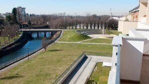 A view of a riverside walkway with a bridge, grassy areas, and a paved path. - Residence Le Groane (Garbagnate Milanese)