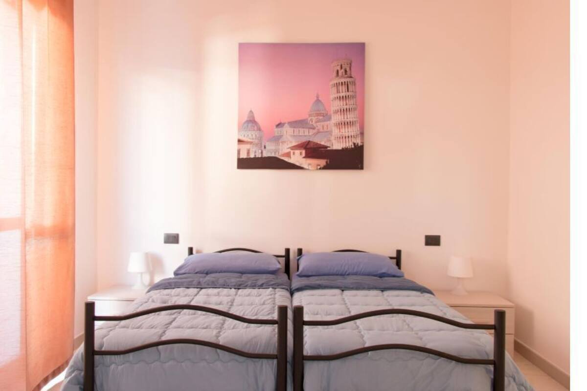 Un lit double avec une tête de lit, une table de chevet et un tableau représentant un bâtiment, accroché au mur.