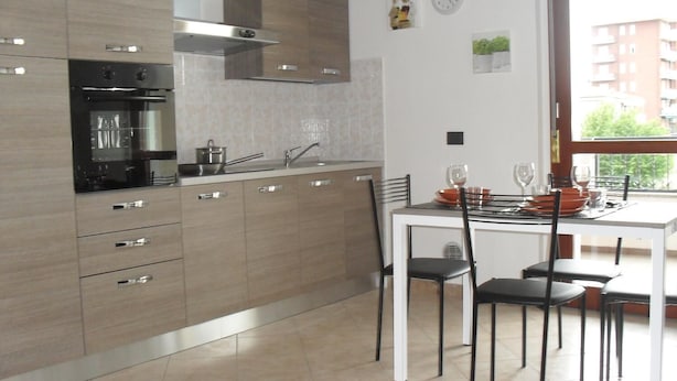 A modern kitchen with a dining area, featuring a stove, sink, cabinets, and a dining table with chairs. - Residence Le Groane (Garbagnate Milanese)