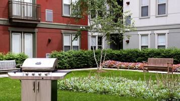 A courtyard with a barbecue grill, a bench, and a small tree.