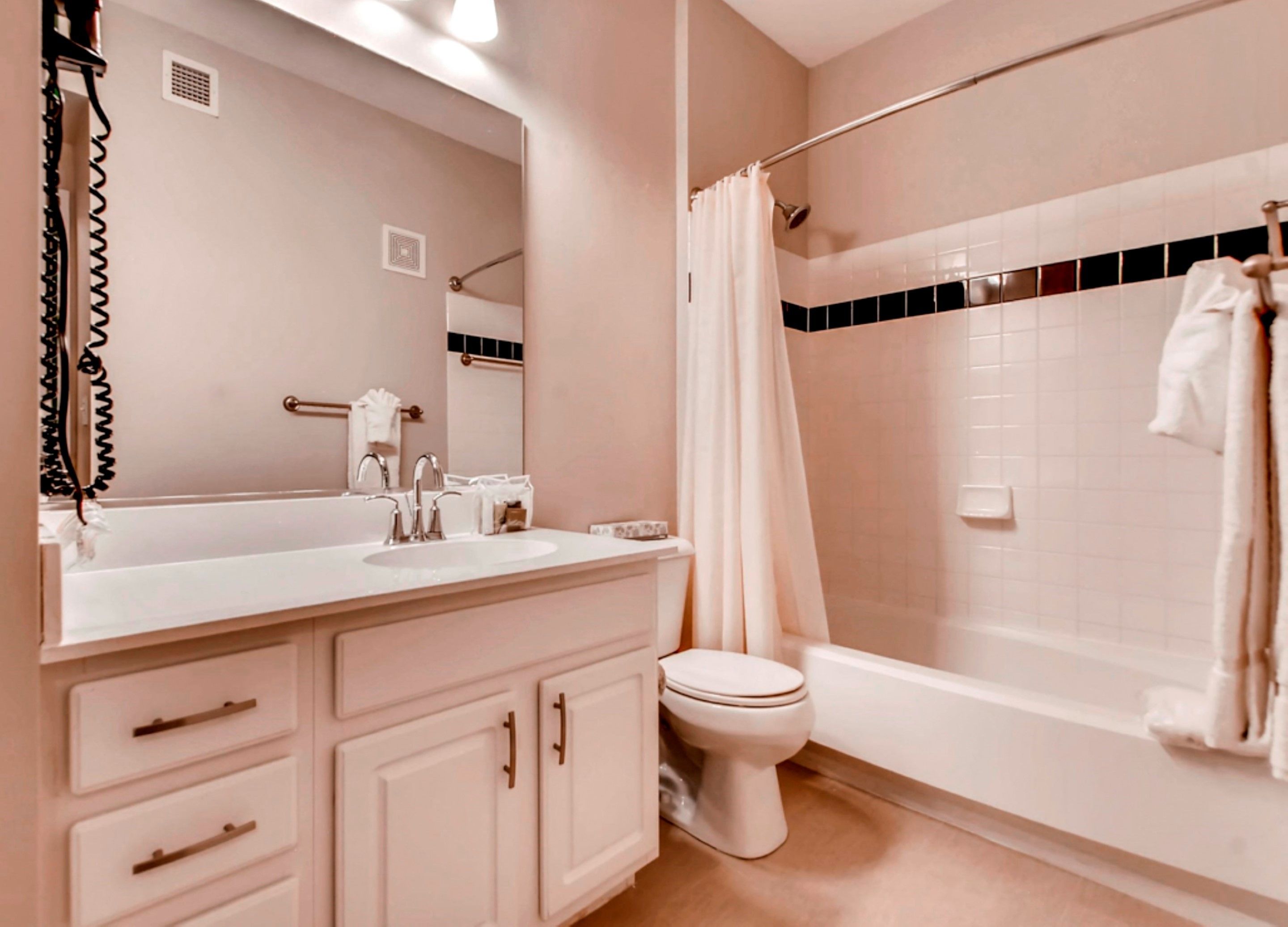 A bathroom with a white sink, mirror, and vanity, a toilet, and a bathtub with a shower curtain.