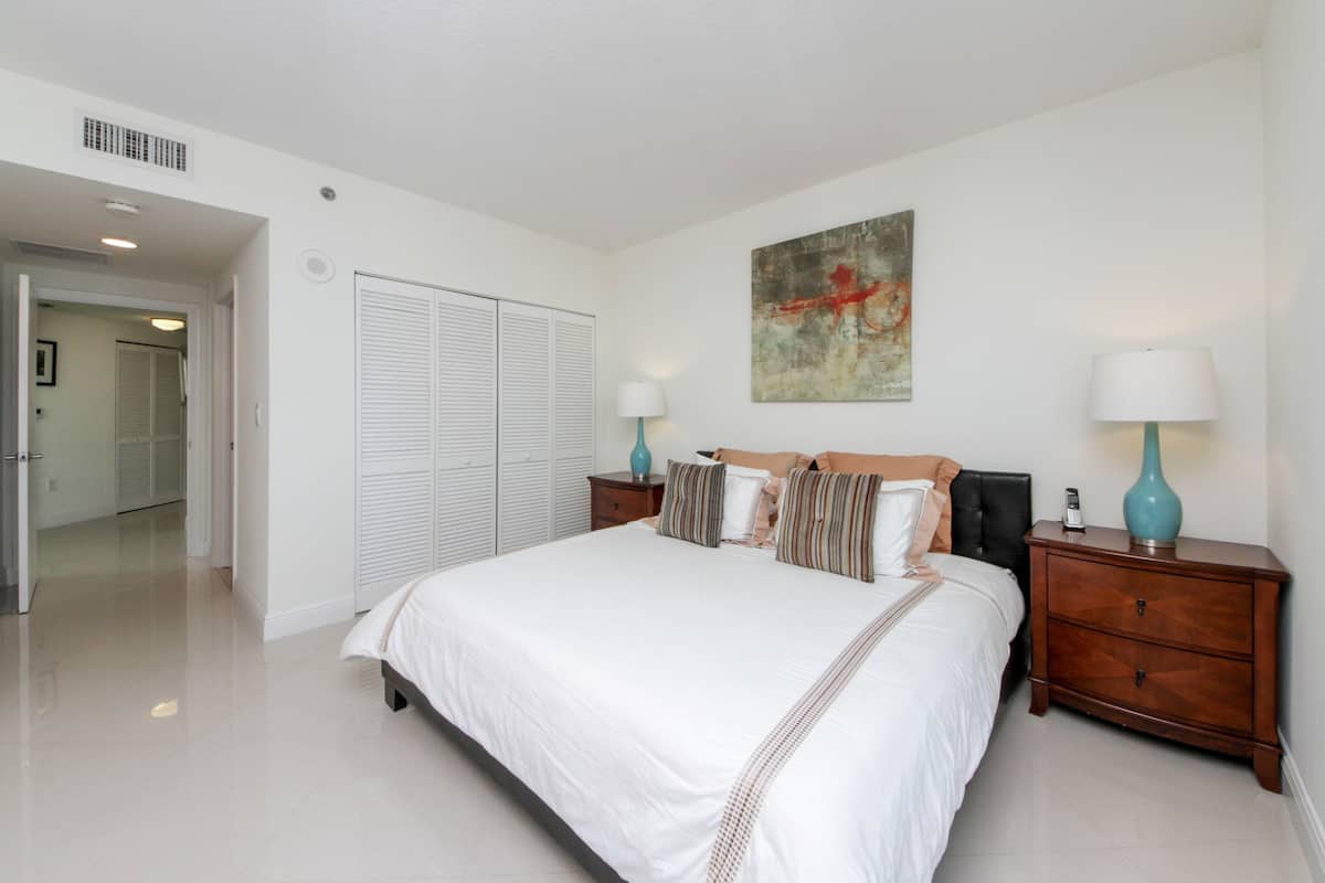 Une chambre spacieuse avec un grand lit, une armoire et deux tables de chevet avec des lampes.