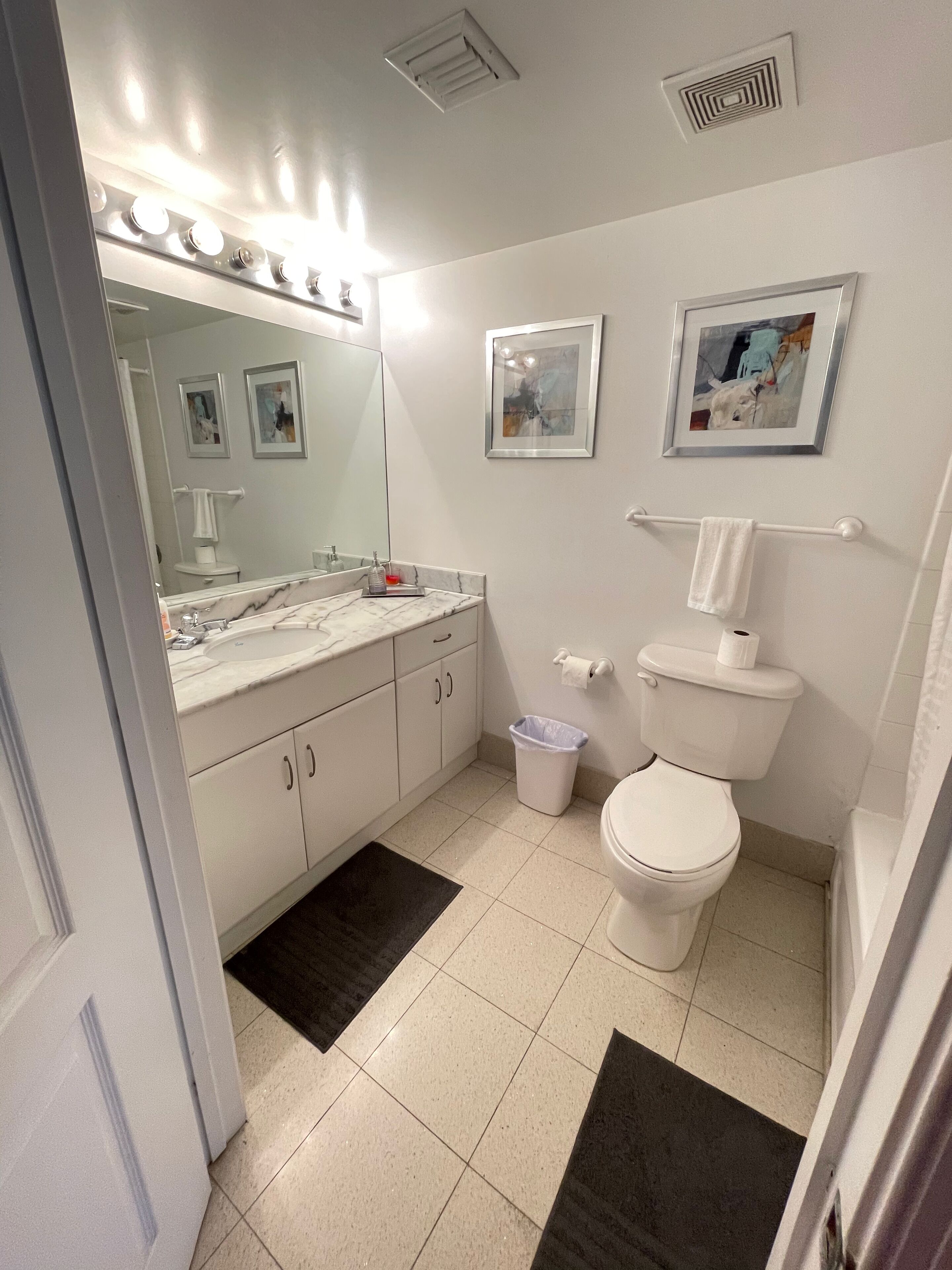 Een moderne badkamer met een witte wastafel, onderkast en toilet. Er hangen twee afbeeldingen aan de muur, een handdoekrek en een prullenbak.