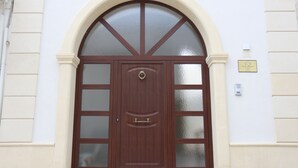 A wooden door with a glass panel and a brass handle, set in a white building with a beige baseboard. - Corte Manzoni B&B (Melendugno)