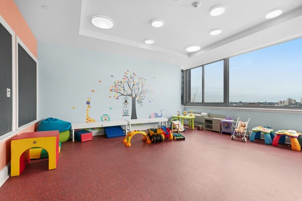 Un salón infantil con juguetes coloridos, un mural y ventanas amplias.