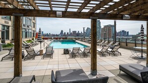A rooftop pool area with lounge chairs and a view of the city skyline. - Bluebird Suites near PATH (Jersey City)
