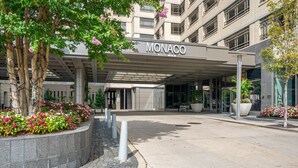 A hotel entrance with a covered walkway, a sign reading "Monaco," and landscaped flower beds. - Bluebird Suites near PATH (Jersey City)
