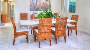 A dining area with wicker chairs, a white table, and a large tropical plant centerpiece. - Secret Cove 1 by Altman (Paynes Bay)