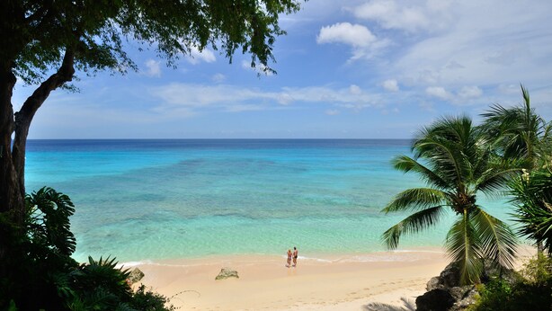 A beach with clear turquoise water, a sandy shore, and a few people walking. - Secret Cove 1 by Altman (Paynes Bay)
