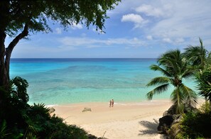 A beach with clear turquoise water, a sandy shore, and a few people walking. - Secret Cove 1 by Altman (Paynes Bay)