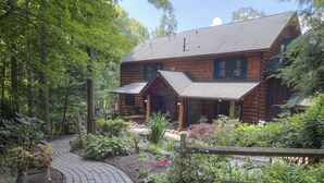 A log cabin with a stone foundation, a covered porch, and a garden with a brick pathway. - Lazy Bear Lodge (Vilas)