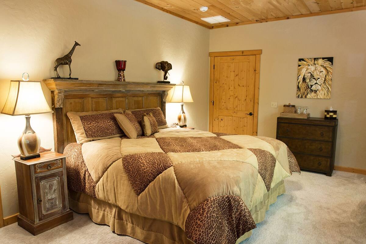 A bedroom with a large bed, two bedside lamps, a wooden headboard, a wooden door, and a painting on the wall.