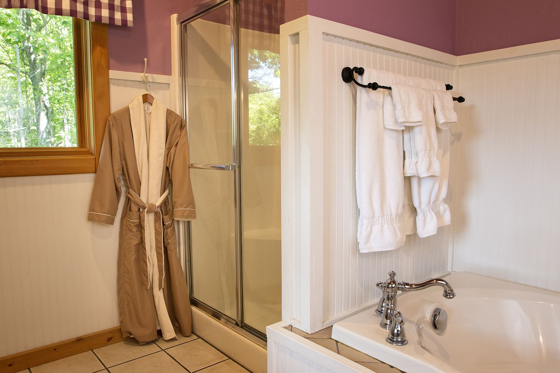 Ein Badezimmer mit einer Duschkabine aus Glas, einer weißen Badewanne und einem Fenster mit Blick auf Bäume.