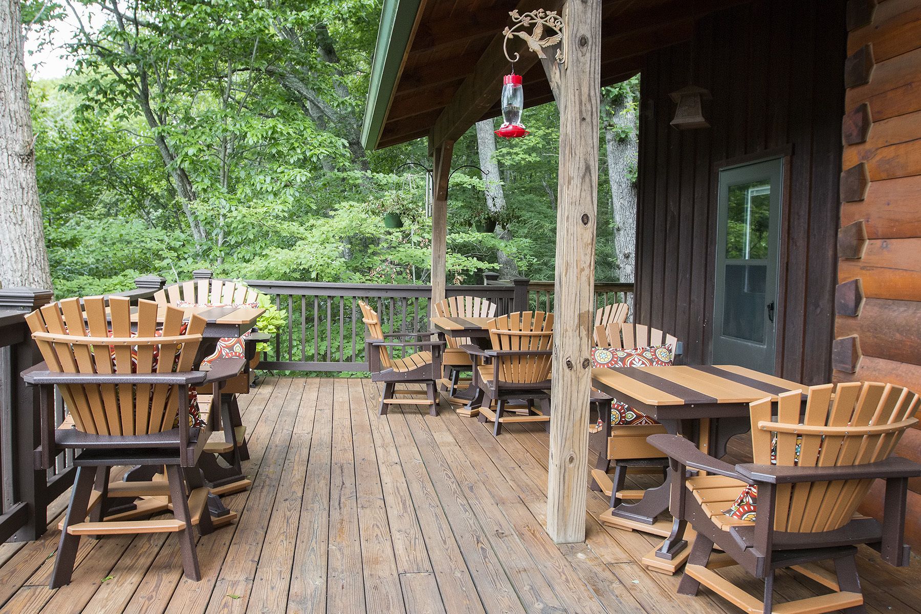 A wooden deck with Adirondack chairs and tables, surrounded by trees.