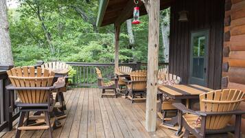 A wooden deck with Adirondack chairs and tables, surrounded by trees.