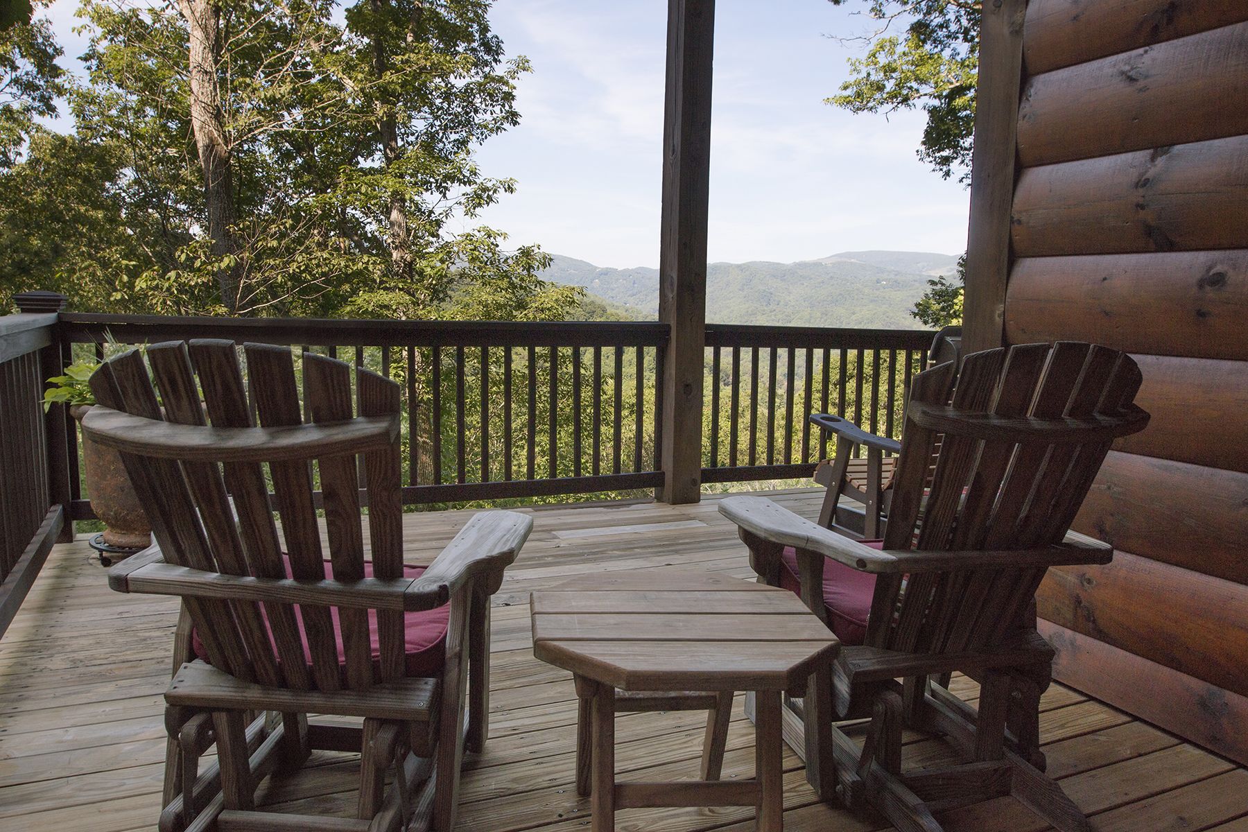 A wooden deck with two Adirondack chairs and a small table, overlooking a mountainous landscape.