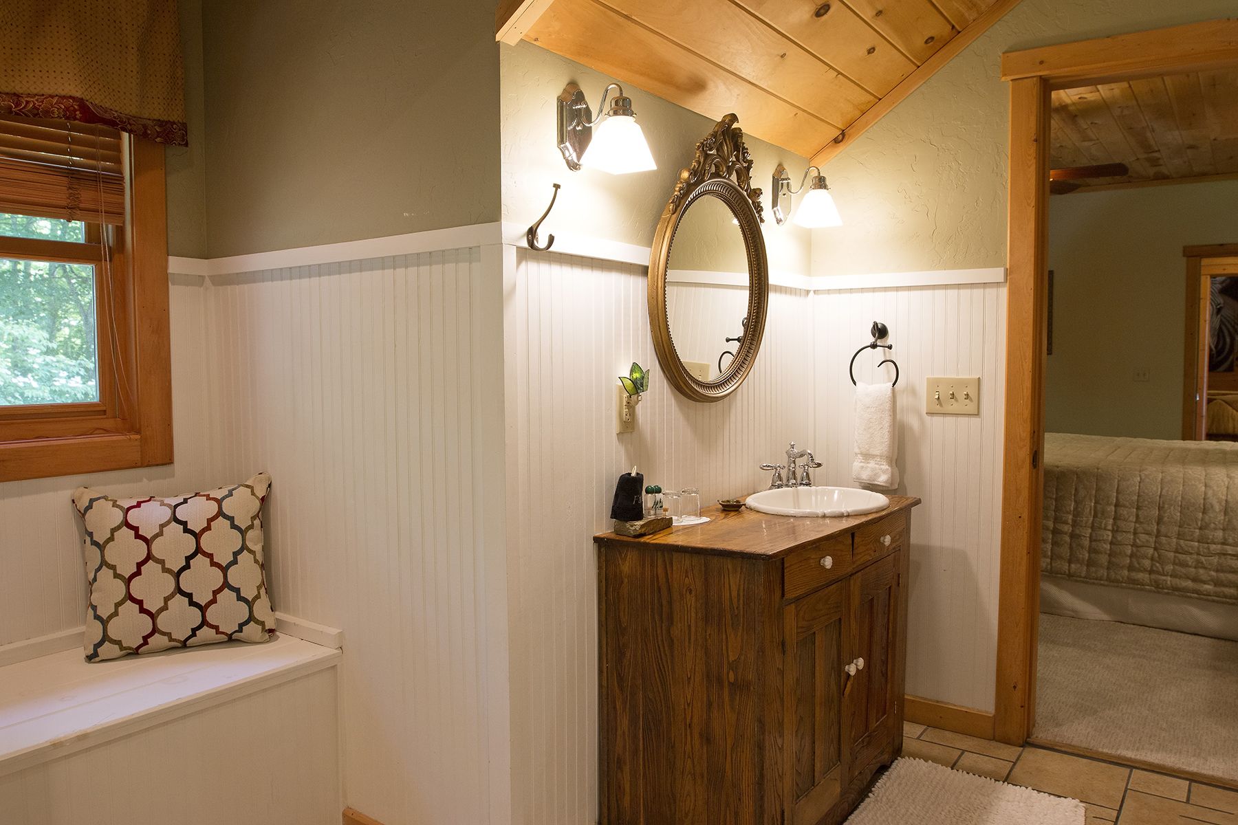 Une salle de bain avec un meuble-lavabo en bois, un grand miroir et une fenêtre avec des stores.