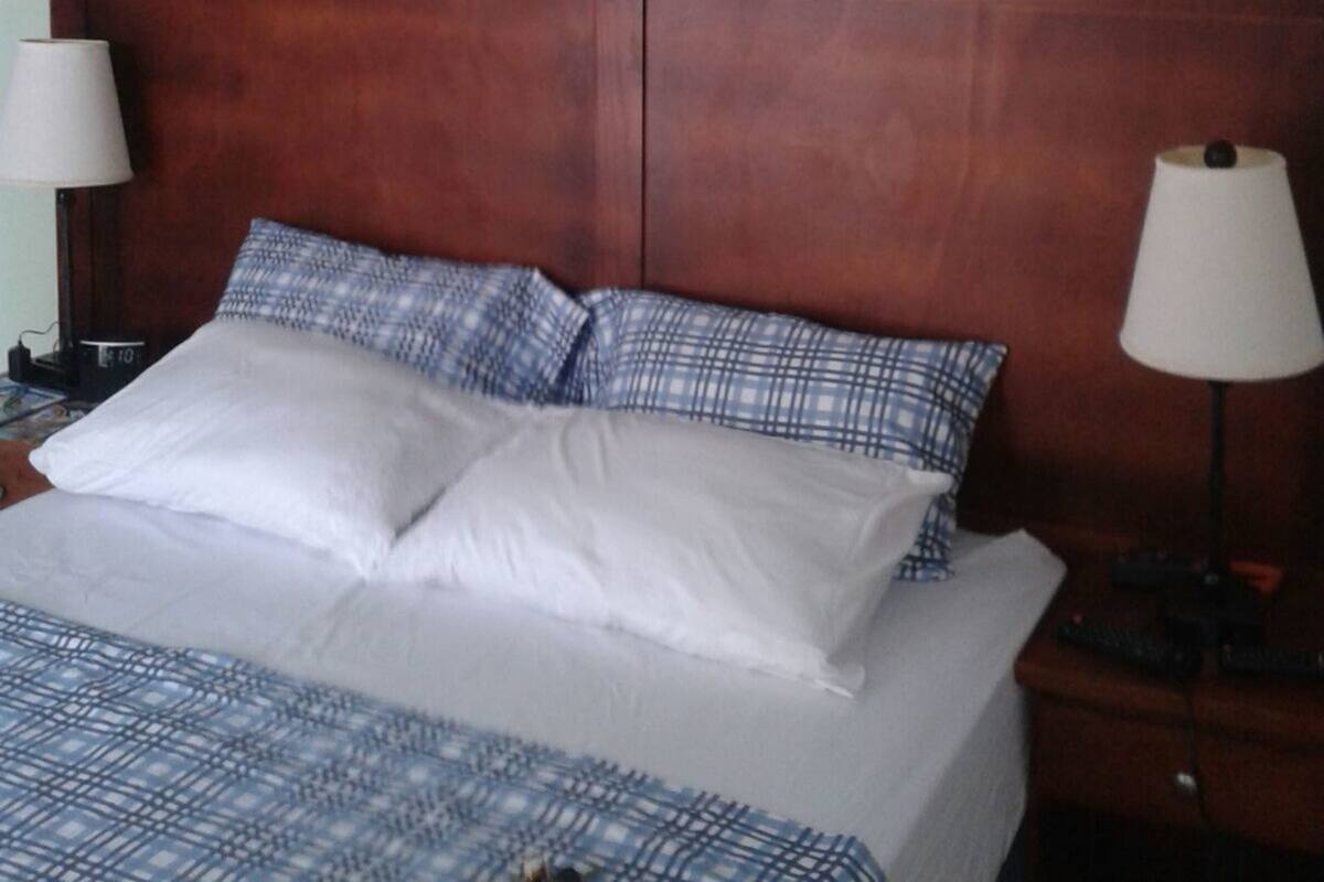 Habitación de hotel con cabecera de madera, cama con ropa de cama a cuadros blancos y azules, dos lámparas de noche y cuadros en las paredes.