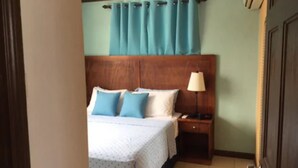A hotel room with a bed, a nightstand, a lamp, and a window with curtains. - Believe Caribbean Apartments (Bridgetown)