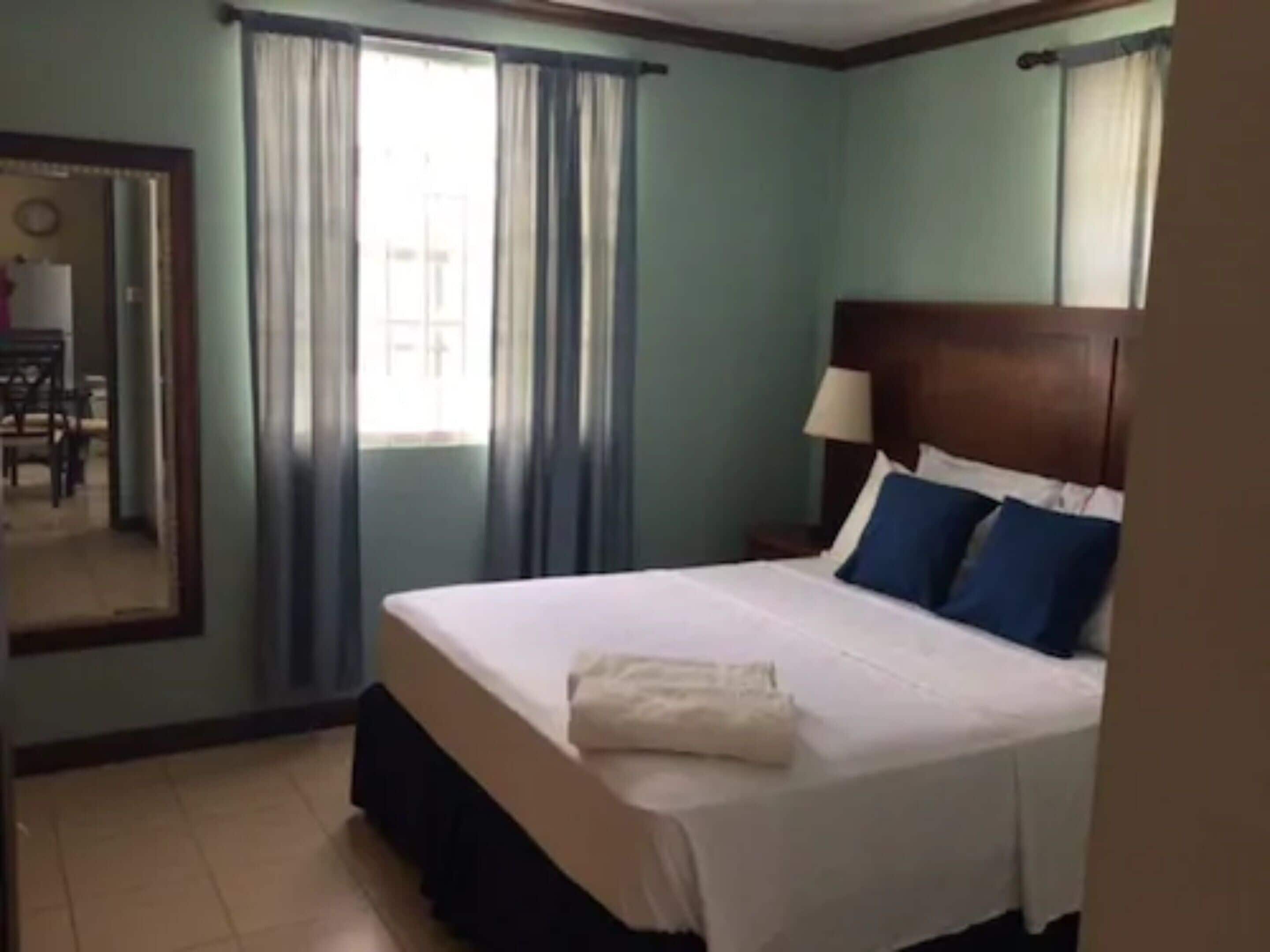 Une chambre d’hôtel avec un lit, une table de chevet, une lampe et une fenêtre avec des rideaux.