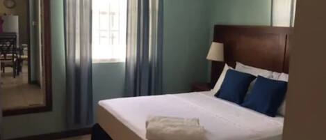 Une chambre d’hôtel avec un lit, une table de chevet, une lampe et une fenêtre avec des rideaux.