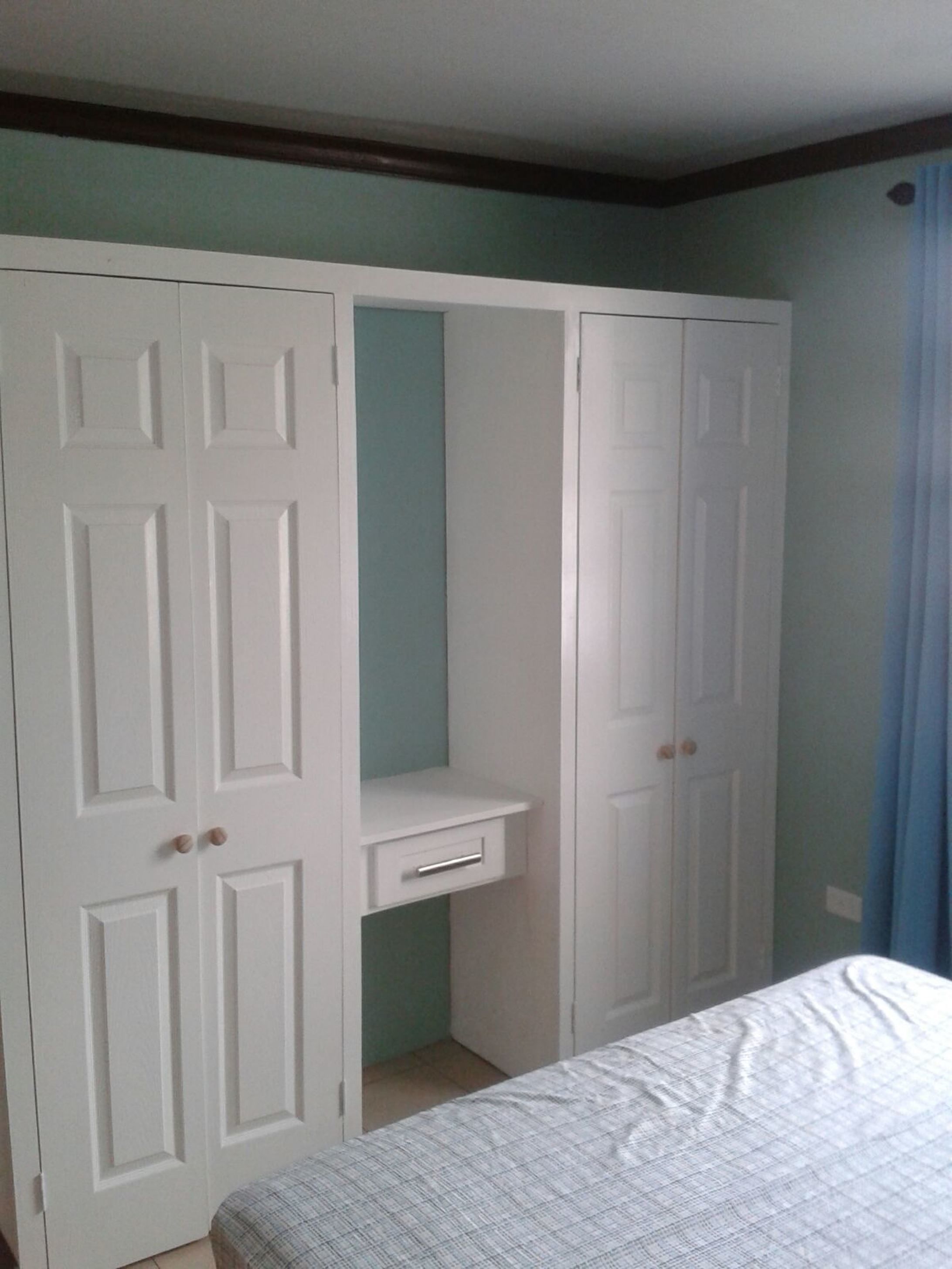 Un dormitorio con una cama, un armario blanco de dos puertas y un escritorio pequeño.