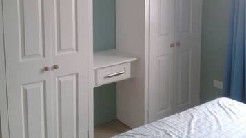 Un dormitorio con una cama, un armario blanco de dos puertas y un escritorio pequeño.