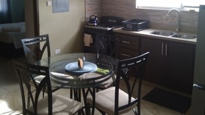 A compact kitchen with a gas stove, a sink, and a dining area with a glass table and chairs. - Believe Caribbean Apartments (Bridgetown)