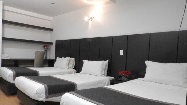 Habitación de hotel con tres camas, una mesita de noche con un jarrón de rosas rojas, y una lámpara de pared.