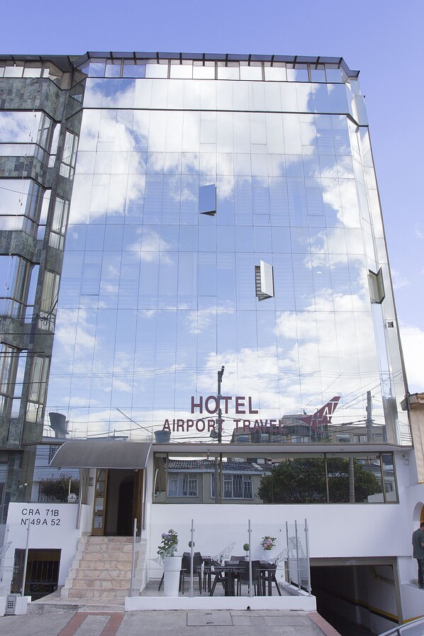 Un hotel moderno con fachada de vidrio reflectante, entrada visible y señal que indica que es un hotel del aeropuerto.