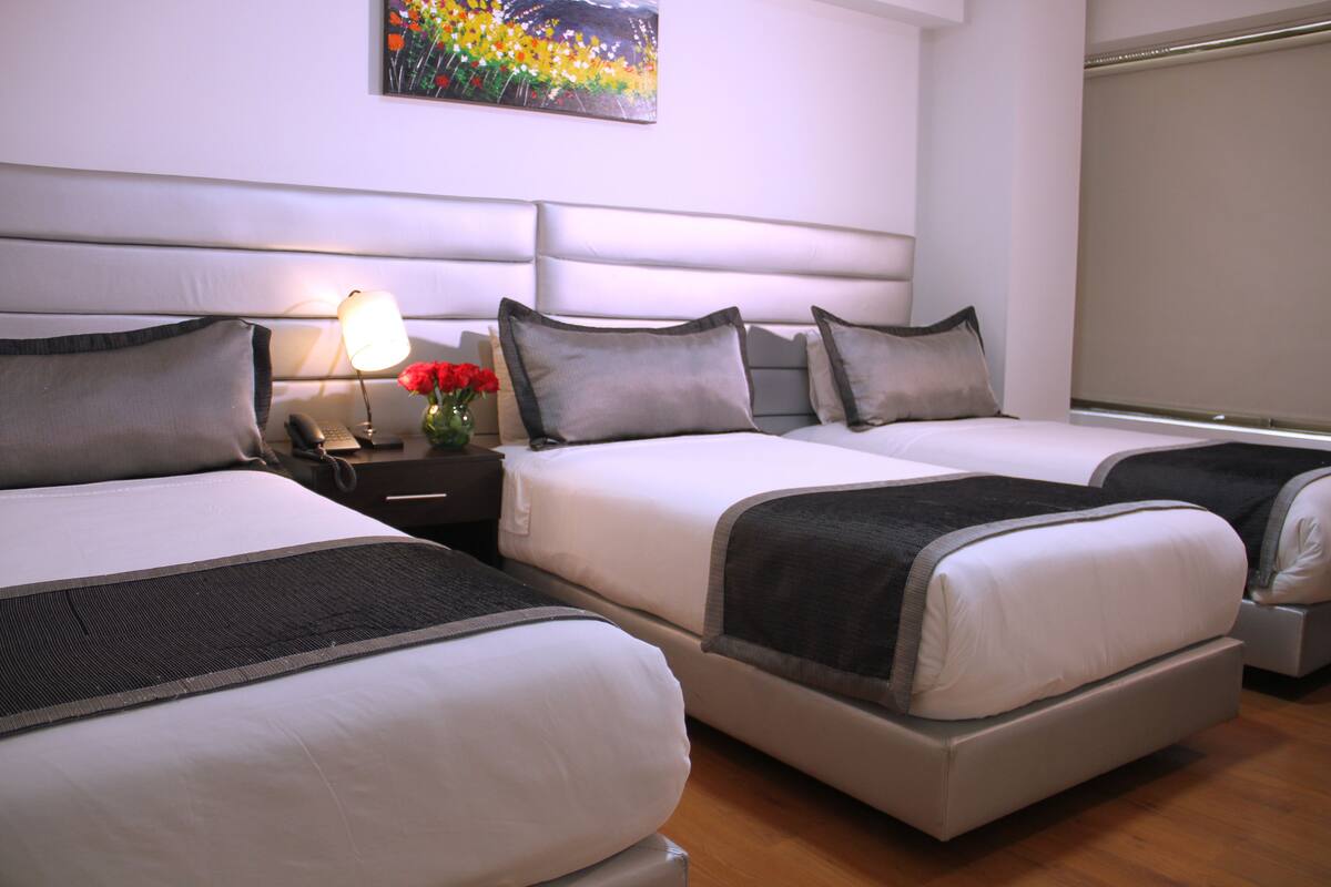 Habitación de hotel con dos camas, una mesita de noche con una lámpara y un florero, y un cuadro en la pared.
