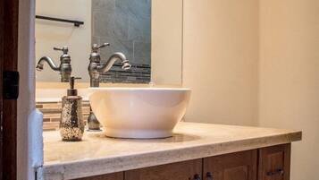 Un baño con un lavabo de pedestal grande, armarios de madera y un espejo sobre el lavabo.