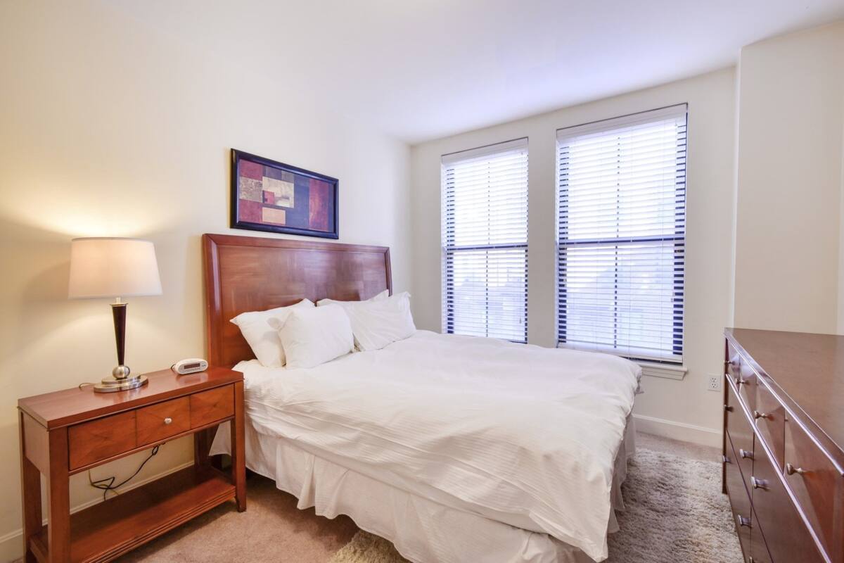 A bedroom with a wooden bed, a nightstand with a lamp, and a dresser.