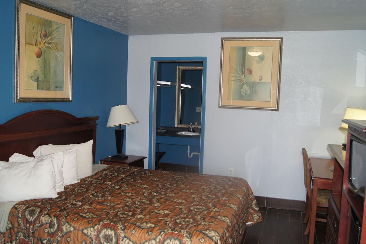 A hotel room with a bed, a desk with a lamp, a television, and two framed pictures on the wall.