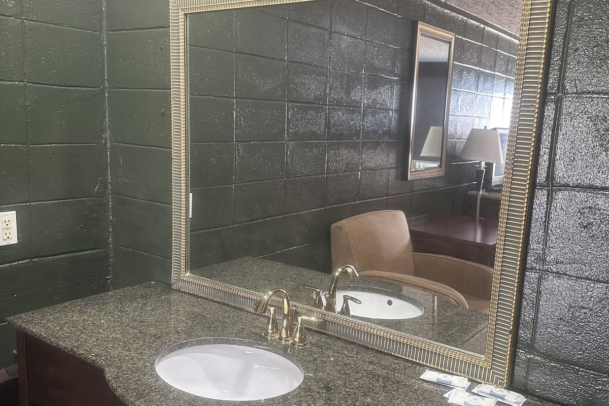 A bathroom with a granite countertop, a sink, a mirror with a gold frame, and a towel dispenser.