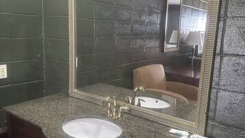 A bathroom with a granite countertop, a sink, a mirror with a gold frame, and a towel dispenser.