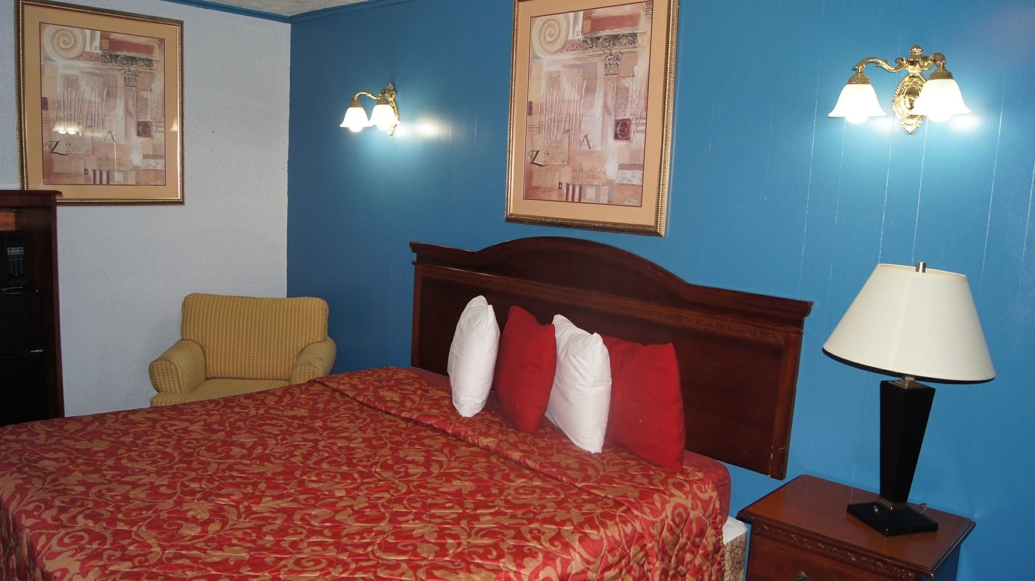 A hotel room with a bed, a chair, a nightstand, and two wall-mounted lamps.