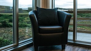 A corner room with a leather chair and large windows offering a view of a grassy landscape. - Afternoon Cottages (Rangárþing ytra)