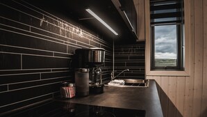 A modern kitchen with black tiled backsplash, stainless steel appliances, and a window with a view of the countryside. - Afternoon Cottages (Rangárþing ytra)