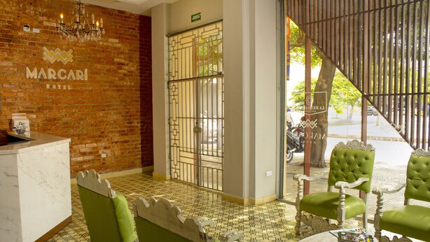 Un hall d’accueil d’hôtel avec un mur en briques, un comptoir d’accueil et des fauteuils recouverts d’un tissu vert.
